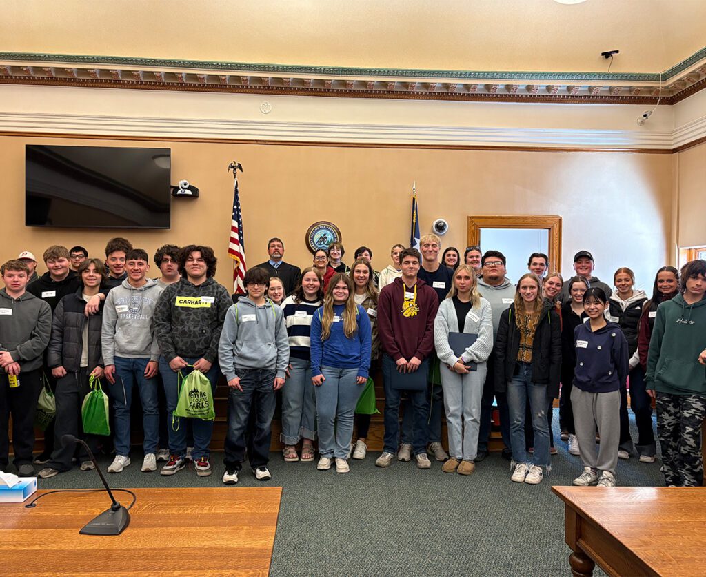 A large group of students posing with a Judge in a courtroom