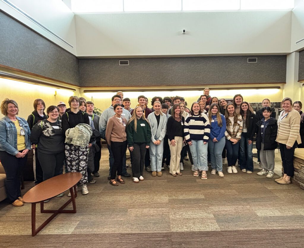 A large group of students posing with staff in a hospital common area